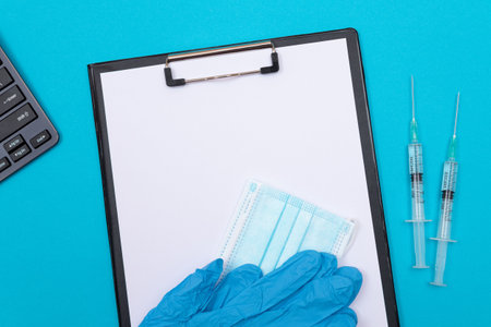 Vaccination, Immunology or Revaccination Concept - Two Medical Syringe Lying on Blue Table in Doctors Office in a Hospital or Clinic. Black Clipboard with Sheet of Paper - Mock Up with Copy Spaceの写真素材