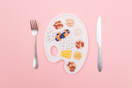 Global Pharmaceutical Industry and Medicinal Products - Different Colored Pills, Tablets and Capsules on White Art Palette with Fork and Knife Lying on Pink Background, Flat Layの写真素材