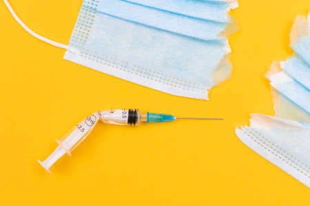 Anti Vaccine Movement and Anti Mask Concept - Broken Medical Syringe and Torn Medical Face Mask Lying on Yellow Background. Pandemic and Lockdown End - Top View, Flat Layの写真素材