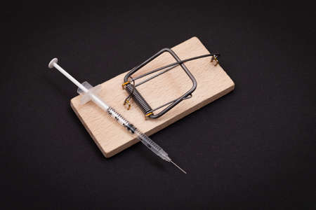 Drug Addict, Heroin Hazard or Dose Trap Concept - Disposable Insulin Syringe with Drug Dose Inside Lying in Wooden Mousetrap on Black Backgroundの写真素材