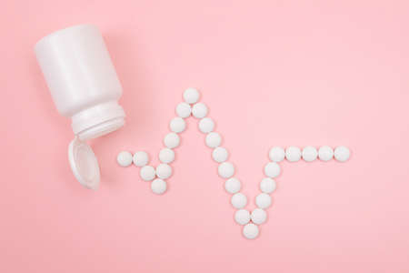 Heartbeat Rhythm. Electrocardiogram. ECG Line Made from White Pills Scattered from the Pill Container, Lying on Pink Background. Global Pharmaceutical Industry and Medicinal Productsの写真素材