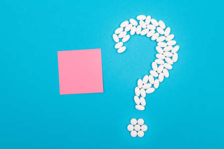 Question Mark Made from White Pills and Tablets with Small Blank Memo Paper, Lying on Blue Background. Global Pharmaceutical Industry and Medicinal Productsの写真素材
