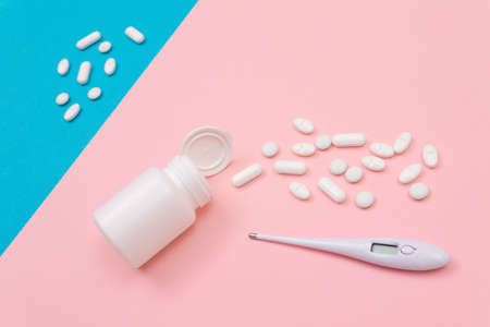 White Pills or Tablets Scattered from the Pill Container with Electronic Thermometer on Split Pink and Blue Background. Pharmaceutical Industry and Medicinal Productsの写真素材