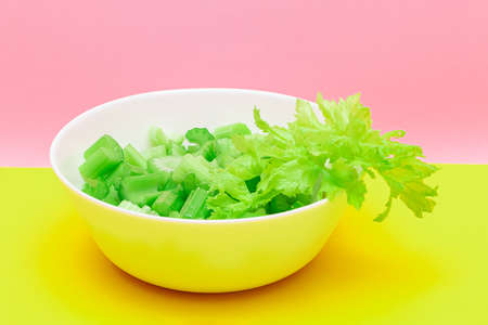 Fresh Chopped Celery Pieces with Water Drops in White Bowl on Yellow Background. Vegan and Vegetarian Culture. Raw Food. Healthy Diet with Negative Calorie Contentの写真素材