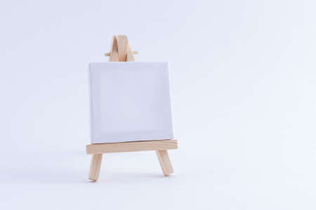 Wooden Easel Miniature with Blank White Square Canvas for Artists and Painters - Mockup. Mini Wooden Stand with Clean Artboard on White Background, Copy Spaceの写真素材
