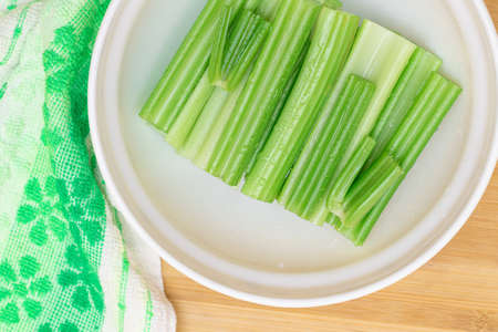 Fresh Chopped Celery Sticks with Water Drops in White Bowl on Bamboo Cutting Board - Top View. Vegan and Vegetarian Culture. Raw Food. Healthy Diet with Negative Calorie Contentの写真素材