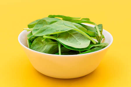 Fresh Baby Spinach Leaves in White Bowl on Yellow Background. Vegan and Vegetarian Culture. Raw...