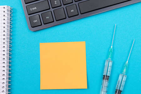 Vaccination, Immunology or Revaccination Concept - Two Medical Disposable Syringe Lying on Blue Table in Doctors Office in a Hospital or Clinic. Blank Orange Sticky Note - Mock Up with Copy Spaceの写真素材