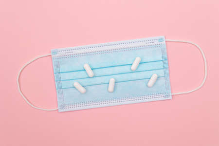 White Pills or Tablets on Medical Face Mask, Lying on Pink Background. Pharmaceutical Industry and...