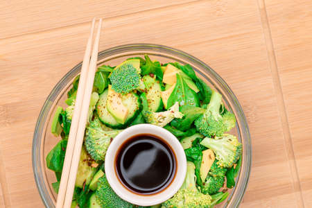Fresh Green Salad of Avocado, Broccoli, Spinach and Cucumber for Detox with Soy Sauce on Wooden Cutting Board. Vegan Salad. Vegetarian Culture. Raw Food. Healthy Eating and Vegetable Dietの写真素材