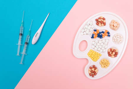 Global Pharmaceutical Industry and Medicinal Products - Different Colored Pills, Tablets and Capsules on White Art Palette with Syringe and Thermometer Lying on Split Blue and Pink Backgroundの写真素材