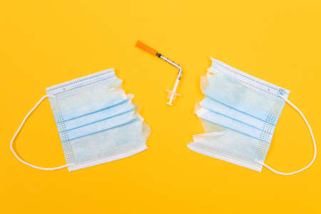 Anti Vaccine Movement and Anti Mask Concept - Broken Medical Syringe and Torn Medical Face Mask Lying on Yellow Background. Pandemic and Lockdown End - Top View, Flat Layの写真素材