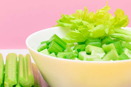 Fresh Chopped Celery Slices in White Bowl with Celery Sticks on White Cutting Board. Vegan and Vegetarian Culture. Raw Food. Healthy Diet with Negative Calorie Contentの写真素材