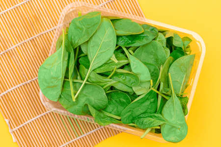 Fresh Baby Spinach Leaves in Transparent Plastic Package on Wooden Mat. Vegan and Vegetarian Culture. Raw Food, Green Leaves. Healthy Dietの写真素材