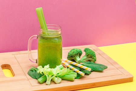Fresh Green Smoothie of Apple, Celery, and Spinach in Glass Smoothie Jar with Yellow Cocktail Straw on Wooden Cutting Board. Vegan Detox Drink. Vegetarian Culture. Healthy Eating and Fruit Dietの写真素材