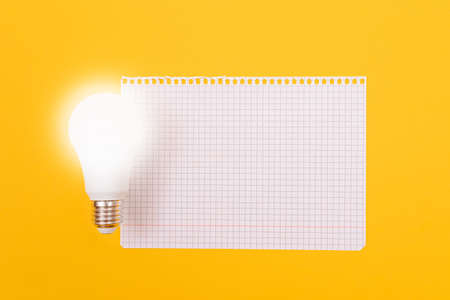 A Power Saving Lamp with Notepad Lying on Yellow Table, Blank Template with Copy Space - Top View, Flat Layの写真素材