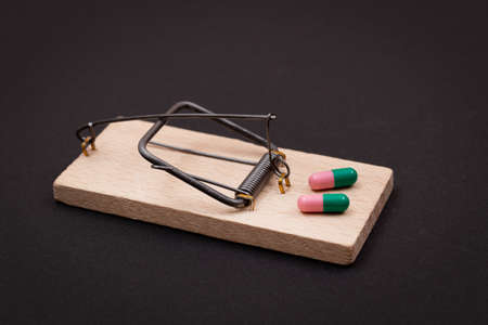 Pharmaceutical Addiction or Big Pharma Trap - Colored Pills or Capsules in Wooden Mousetrap on Black Backgroundの写真素材