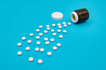 Global Pharmaceutical Industry and Medicinal Products - White Pills or Tablets Scattered from the Bottle, Lying on Blue Backgroundの写真素材
