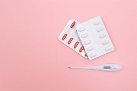 Different Pills and Tablets Package with White Electronic Thermometer on Pink Background. Pharmaceutical Industry and Medicinal Products. Top View, Flat Layの写真素材