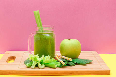 Fresh Green Smoothie of Apple, Celery, and Spinach in Glass Smoothie Jar with Yellow Cocktail Straw on Wooden Cutting Board. Vegan Detox Drink. Vegetarian Culture. Healthy Eating and Fruit Dietの写真素材