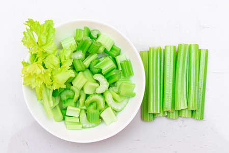 Fresh Chopped Celery Sticks and Slices with Water Drops in White Bowl on White Cutting Board - Top View. Vegan and Vegetarian Culture. Raw Food. Healthy Diet with Negative Calorie Contentの写真素材