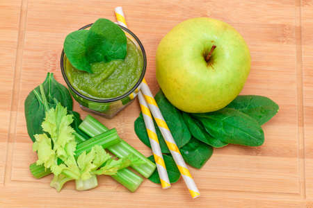 Fresh Green Smoothie of Apple, Celery, and Spinach in Glass Beaker with Yellow Cocktail Straw on Wooden Cutting Board. Vegan Detox Drink. Vegetarian Culture. Healthy Eating and Fruit Dietの写真素材