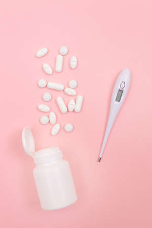 White Pills or Tablets with Electronic Thermometer on Pink Background. Pharmaceutical Industry and...