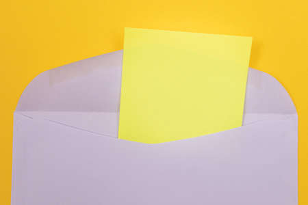 Violet Envelope with Blank Yellow Sheet of Paper Inside, Lying on Yellow Background - Mock Up with Copy Space. Receiving Mail or Notice, Sending Postcard - Top View, Flat Layの写真素材