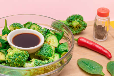 Fresh Green Salad of Avocado, Broccoli, Spinach and Cucumber with Soy Sauce and Red Hot Pepper on Wooden Cutting Board. Vegan Salad. Vegetarian Culture. Raw Food. Healthy Eating and Vegetable Dietの写真素材