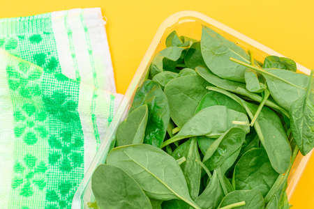 Fresh Baby Spinach Leaves in Transparent Plastic Package on Yellow Background - Top View. Vegan and Vegetarian Culture. Raw Food, Green Leaves. Healthy Dietの写真素材
