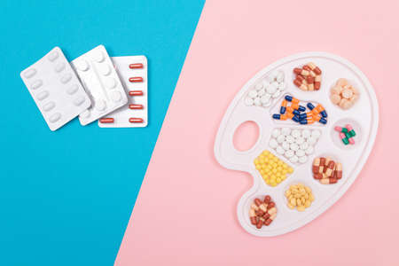 Global Pharmaceutical Industry and Medicinal Products - Different Colored Pills, Tablets and Capsules on White Art Palette with Pill Packages Lying on Split Blue and Pink Background, Flat Layの写真素材