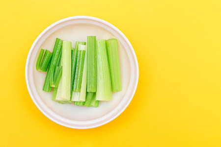 Fresh Chopped Celery Sticks with Water Drops in White Bowl on Yellow Background - Top View. Vegan and Vegetarian Culture. Raw Food. Healthy Diet with Negative Calorie Contentの写真素材