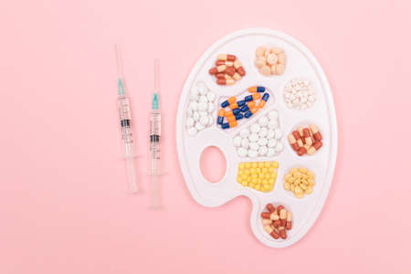 Global Pharmaceutical Industry and Medicinal Products - Different Colored Pills, Tablets and Capsules on White Art Palette with Syringe Lying on Pink Background, Flat Layの写真素材