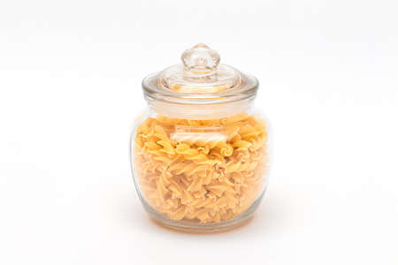 Uncooked Fusilli Pasta in Glass Jar on White Background. Raw and Dry Macaroni. Unhealthy and Fat Food. Italian Cultureの写真素材