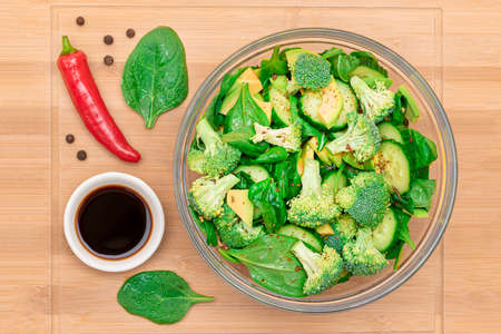 Fresh Green Salad of Avocado, Broccoli, Spinach and Cucumber with Soy Sauce and Red Hot Pepper on Wooden Cutting Board. Vegan Salad. Vegetarian Culture. Raw Food. Healthy Eating and Vegetable Dietの写真素材