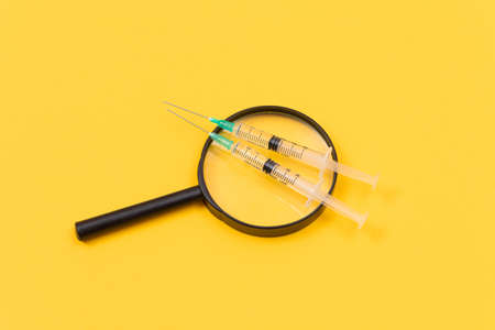 A Magnifier with Medical Syringe Lying on Yellow Table - Vaccination Conceptの写真素材