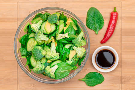 Fresh Green Salad of Avocado, Broccoli, Spinach and Cucumber with Soy Sauce and Red Hot Pepper on Wooden Cutting Board. Vegan Salad. Vegetarian Culture. Raw Food. Healthy Eating and Vegetable Dietの写真素材