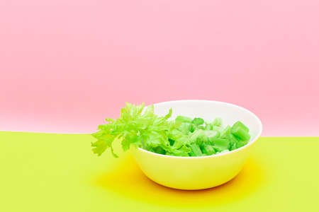 Fresh Chopped Celery Pieces with Water Drops in White Bowl on Yellow Background. Vegan and Vegetarian Culture. Raw Food. Healthy Diet with Negative Calorie Contentの写真素材