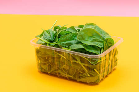 Fresh Baby Spinach Leaves in Transparent Plastic Package on Yellow Background. Vegan and Vegetarian Culture. Raw Food, Green Leaves. Healthy Dietの写真素材