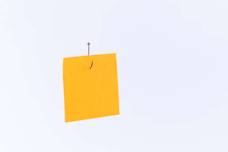 Mockup of a Blank Orange Memo Paper with Copy Space Hanging on a Fishing Hook Against the White Background. Reminder or To Do List. Sticky Note Templateの写真素材