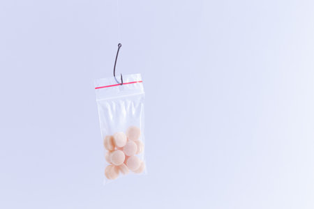 The Pharmaceutical Trap and Drug Addiction - Colored Pills or Tablets Hanging in Small Ziplock Bag on a Fishing Hook Against the White Backgroundの写真素材