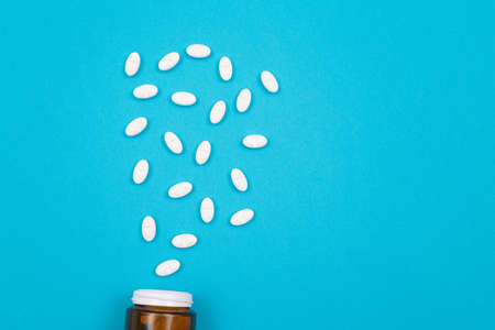 Global Pharmaceutical Industry and Medicinal Products - White Pills or Tablets Scattered from the Pill Container, Lying on Blue Backgroundの写真素材