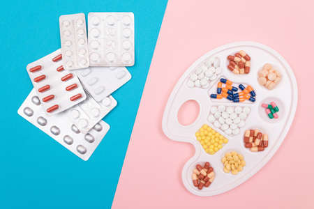 Global Pharmaceutical Industry and Medicinal Products - Different Colored Pills, Tablets and Capsules on White Art Palette with Pill Packages Lying on Split Blue and Pink Background, Flat Layの写真素材