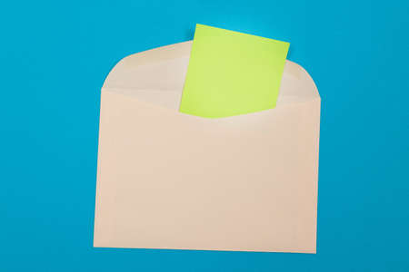Beige Envelope with Blank Green Sheet of Paper Inside, Lying on Blue Background - Mock Up with Copy Space. Receiving Mail or Notice, Sending Postcard - Top View, Flat Layの写真素材