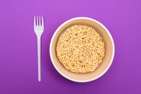 Opened Package with Uncooked Instant Noodles on Violet Background. Raw Pasta. Dry Asian Fast Food. Quick Lunchの写真素材