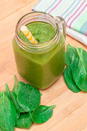 Fresh Green Smoothie of Apple, Celery, and Spinach in Glass Smoothie Jar with Yellow Cocktail Straw on Wooden Cutting Board. Vegan Detox Drink. Vegetarian Culture. Healthy Eating and Fruit Dietの写真素材