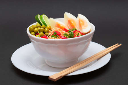 Beautiful Noodle Dish with Green Pea, Eggs, Red Hot Pepper, Greens and Lime with Chopsticks on Black Background. Instant Noodlesの写真素材