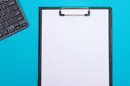 Black Clipboard with Blank White Sheet of Paper Lying on Blue Table - Top View, Flat Layの写真素材