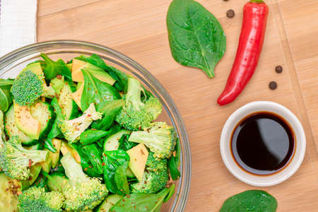 Fresh Green Salad of Avocado, Broccoli, Spinach and Cucumber with Soy Sauce and Red Hot Pepper on Wooden Cutting Board. Vegan Salad. Vegetarian Culture. Raw Food. Healthy Eating and Vegetable Dietの写真素材