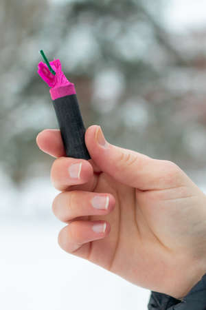 Firecracker in a Hand. Guy Holding a Petard Outdoors in Winter at Daytime. Loud and Dangerous New Years Entertainment. Hooliganism with Pyrotechnics. Noise of Firecrackers in Public Placesの写真素材